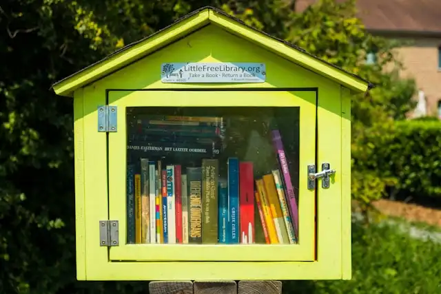 A Little Free Library. It is designed to look like a small yellow house. There is a glass door, revealing many books inside. There is a banner that says "LittleFreeLibrary.org Take a Book Leave a Book."